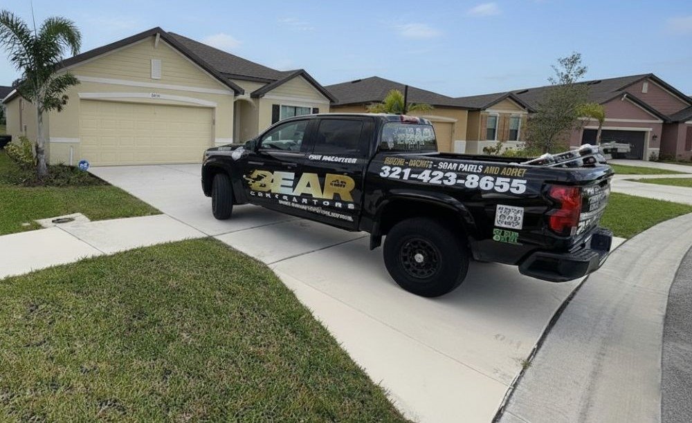 A black pickup truck, branded with "BEAR CONTRACTORS" and a phone number, is parked in the driveway of a beige suburban home in a neighborhood street.